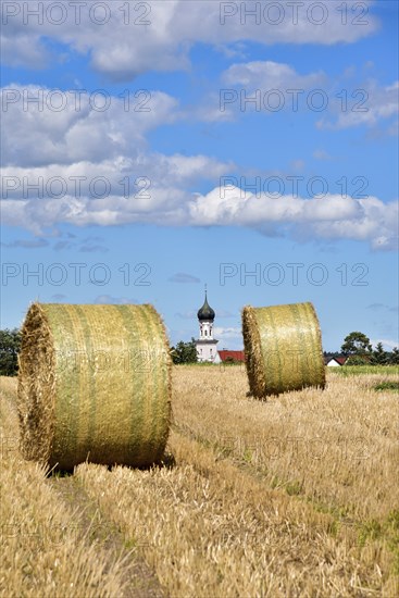 Straw bales on a harvested grain field, in the background the village church with onion tower,