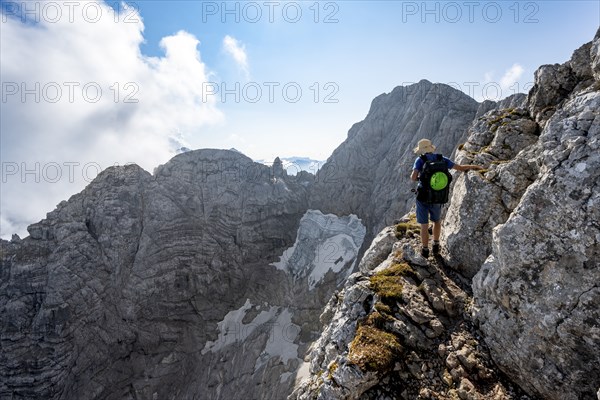 Mountaineer on a rocky narrow mountain path, view of rock faces with blue ice glacier and summit of
