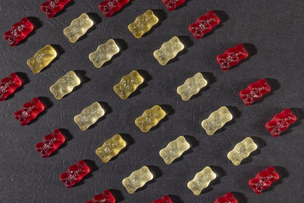 Different coloured gummy bears in rows, on a dark background