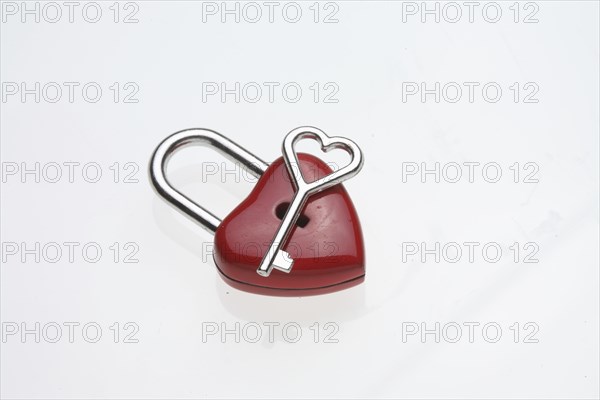 Small heart-shaped key lies on a red padlock
