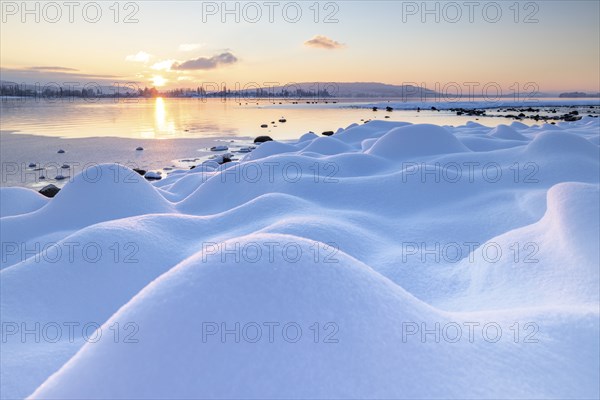 Gentle hills of snow stretch towards the lake, where the sun sets over the mountains, Seegarten,