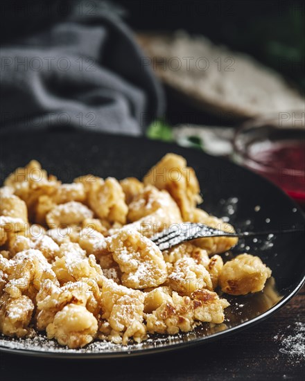 Close-up of Kaiserschmarrn on a black plate, dusted with sugar, jam in the background, dark