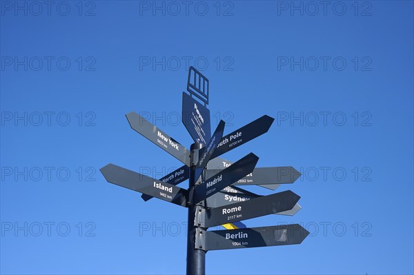 Black signpost against a blue sky with directions to various towns and destinations, Fløibanen