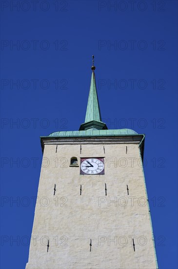 Historic church tower with green copper spire and built-in clock in front of a clear blue sky,