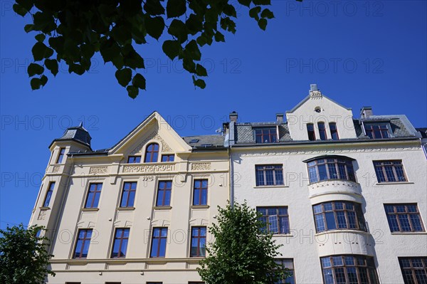 A historic building with an elaborate façade and many windows, surrounded by green trees under a