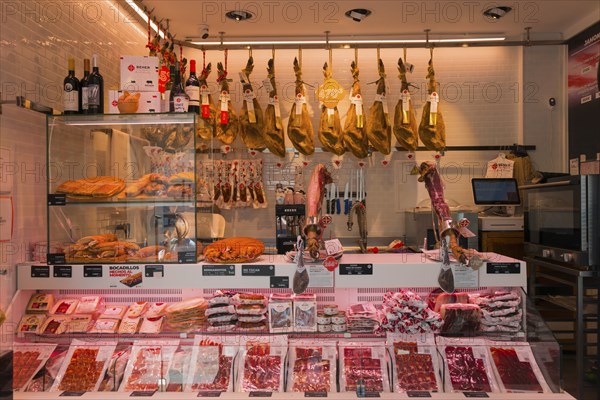 Modern butcher's shop with meat counter, hanging hams, sausages and wine bottles on display,