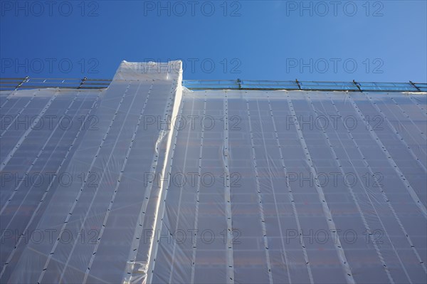 Shielding of a building by a tarpaulin attached to scaffolding against a clear blue sky, Bergen,