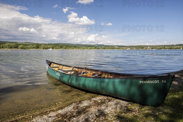 Green canoe on the shore of a lake with clear water and cloudy sky, quiet peaceful surroundings,