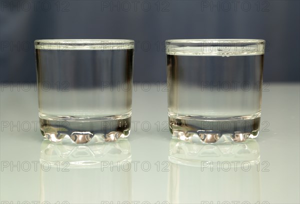 Two glasses filled with vodka standing on a glass table