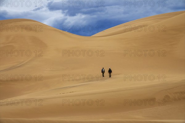 Two travelers in the desert. Hiking on sand dunes in mountains. Gobi desert, Mongolia, Asia