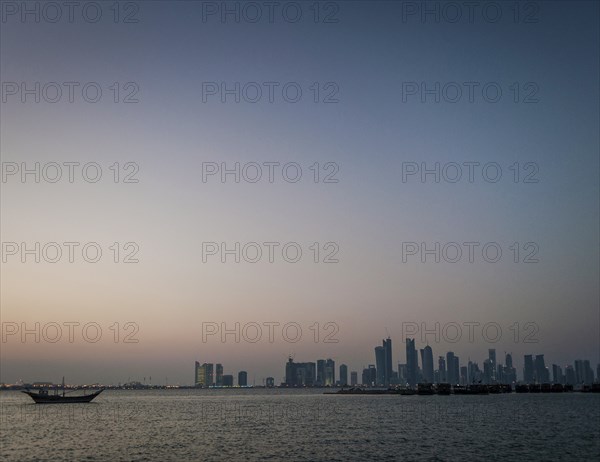 Doha city skyscrapers urban skyline view and dhow boat in qatar at sunset