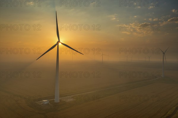 Beautiful aerial sunset landscape with windmills or wind turbine on wind farm in rotation to