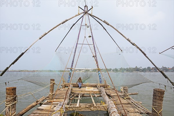 Indian fisherman sitting on a Chinese fishing net, behind him the Arabian Sea, Kochi, Kerala,