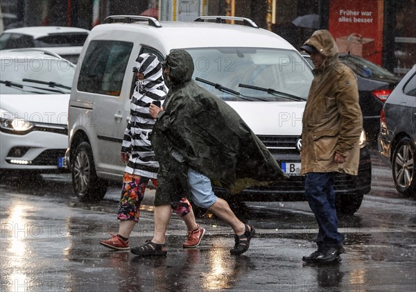 People in rain gear walking across a street in heavy rainfall, Berlin, 23 06 2023