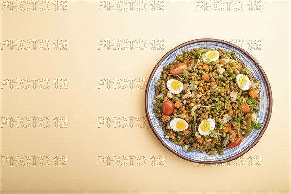 Mung bean porridge with quail eggs, tomatoes and microgreen sprouts on a pastel orange background.