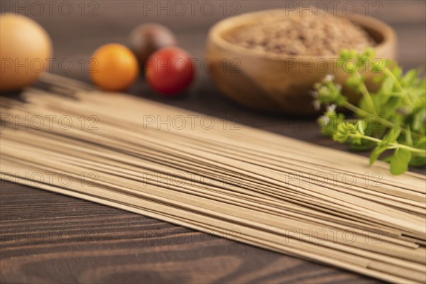 Japanese buckwheat soba noodles with tomato, eggs, spices, herbs on brown wooden background. Side