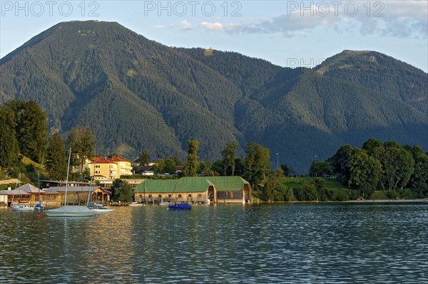 Tegernsee with sailing boats and boat huts, warm evening light, town Tegernsee, mountain Wallberg,