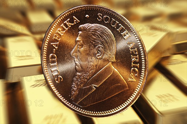Close-up of a Krugerrand gold coin, in the background blurred gold bars (composing)