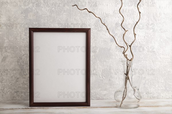 Brown wooden frame mockup with dried wine branch in glass on gray concrete background. Blank,