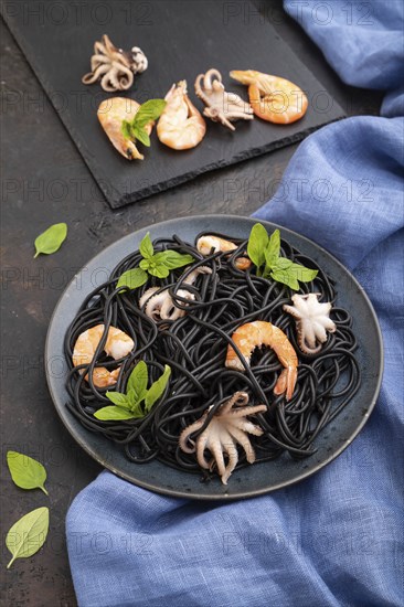 Black cuttlefish ink pasta with shrimps or prawns and small octopuses on black concrete background