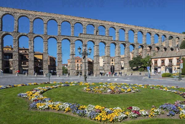 A historic stone aqueduct with arches spans a city under a bright blue sky next to a colourful