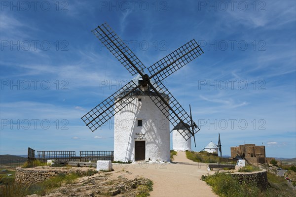 White windmill in front of a blue sky with few clouds, surrounded by nature and historical