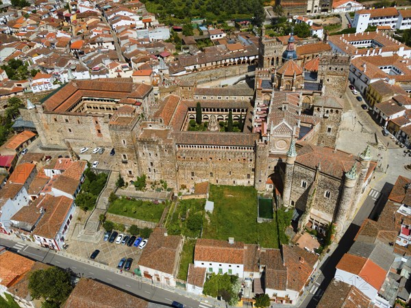 Aerial view of an old monastery with courtyard and red roofs, surrounded by a village in Spain.