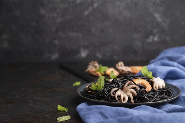Black cuttlefish ink pasta with shrimps or prawns and small octopuses on black concrete background