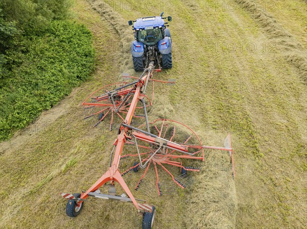 Aerial view of a tractor with hay machine in a field, surrounded by cut grass and hay bales,