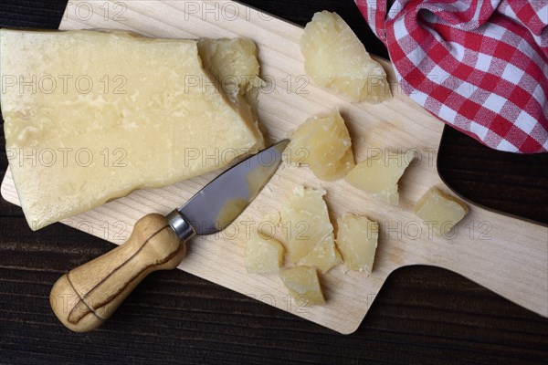 A piece of Parmesan cheese and chopped pieces of cheese on a wooden board