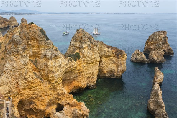 Rugged cliffs and rocks rise from the crystal clear water near sailing boats, Ponta da Piedade,