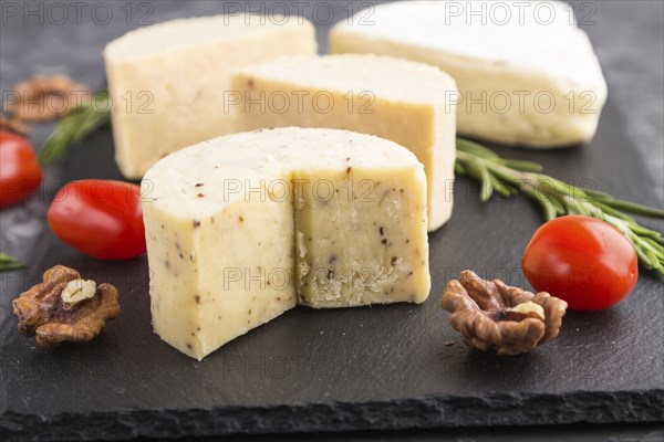 Cheddar cheese and various types of cheese with rosemary and tomatoes on black slate board on a