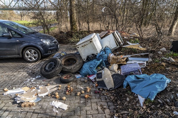 Illegal waste disposal in a car park, in a wooded area, tyres, furniture, refrigerators, household