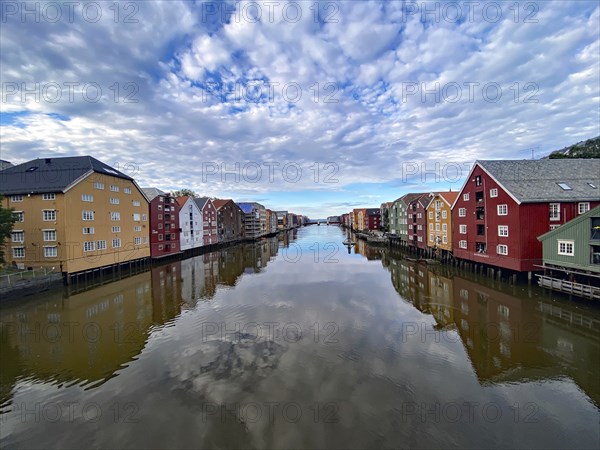 River reflecting colourful wooden buildings under a cloudy blue sky, calm atmosphere, view from the