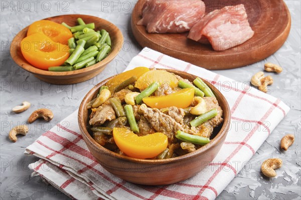 Fried pork with peaches, cashew and green beans on a black concrete background. side view, close