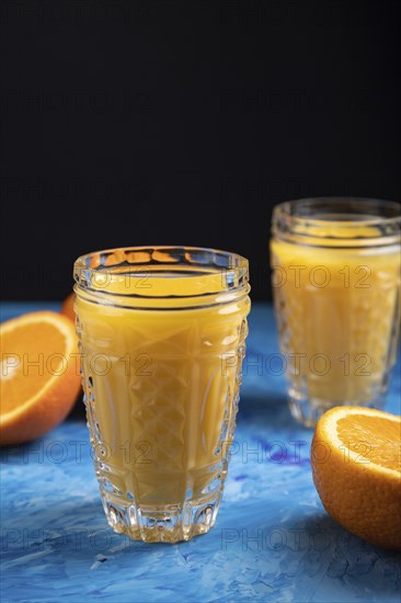 Glass of orange juice on a black and blue background. Hard light, contrast. Side view, close up