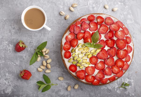 Homemade cake with yoghurt cream, strawberry, pistachio and a cup of coffee on a gray concrete