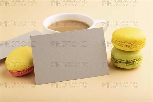 Gray paper business card mockup with yellow and green macaroons and cup of coffee on orange pastel