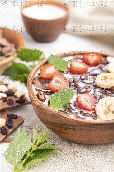 Chocolate cornflakes with milk and strawberry in wooden bowl on white wooden background and linen