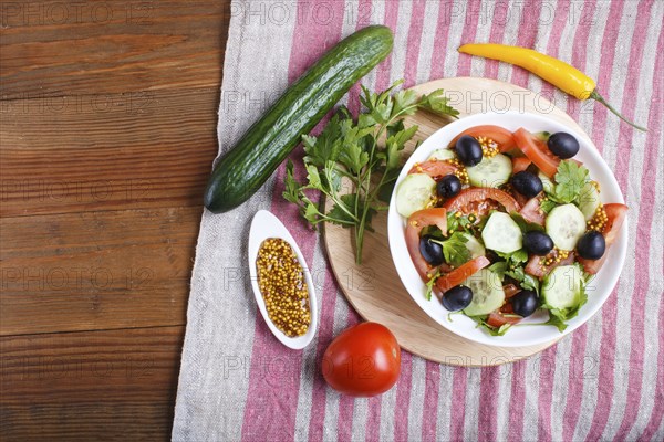 Vegetarian salad of tomatoes, cucumbers, parsley, olives and mustard on linen tablecloth, top view,