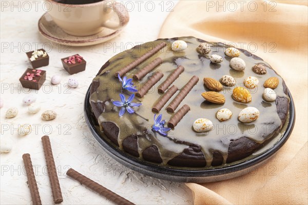 Homemade chocolate brownie cake with caramel cream and almonds with cup of coffee on a white