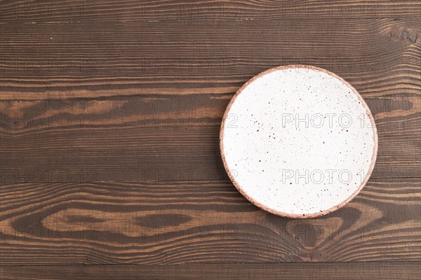 Empty white with dots ceramic plate on brown wooden background. Top view, copy space, flat lay