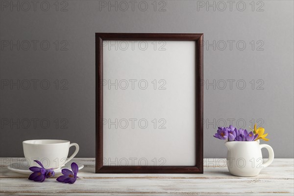 Brown wooden frame mockup with snowdrop crocus flowers and white coffee cup on gray paper