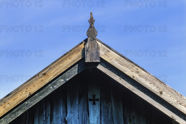 Roof ridge on an old wooden house with joinery and a cross on the gable