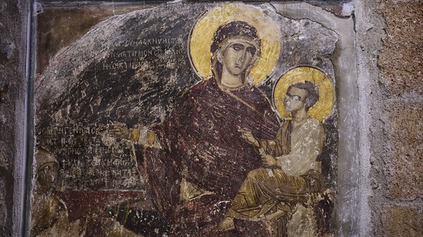 A detail of a medieval fresco showing a saint with a halo holding a child against a weathered