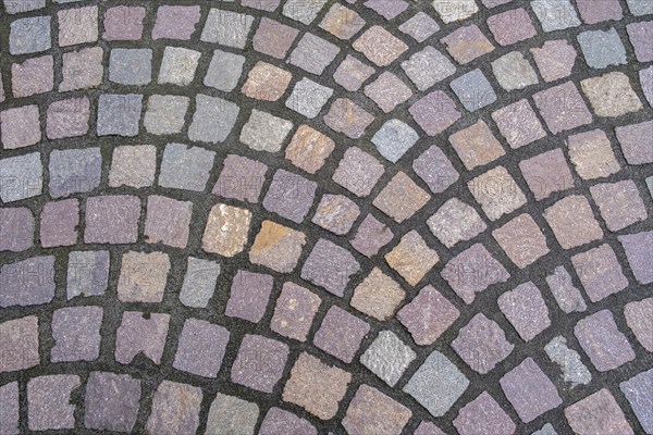Pavement made of irregularly arranged, square paving stones in shades of grey, purple and brown,