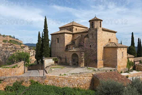 A medieval stone church surrounded by cypress trees in a tranquil Mediterranean landscape under a