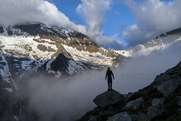 Silhouette of a mountaineer in front of a cloudy, atmospheric mountain landscape, rocky