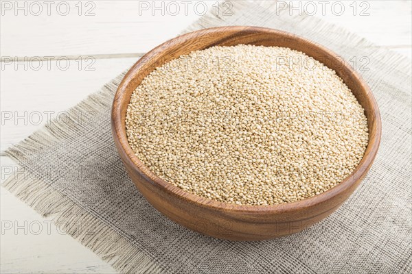 Wooden bowl with raw white quinoa seeds on a white wooden background and linen textile. Side view,