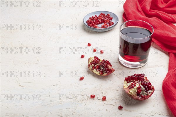 Glass of pomegranate juice on a white concrete background with red textile. Side view, copy space,
